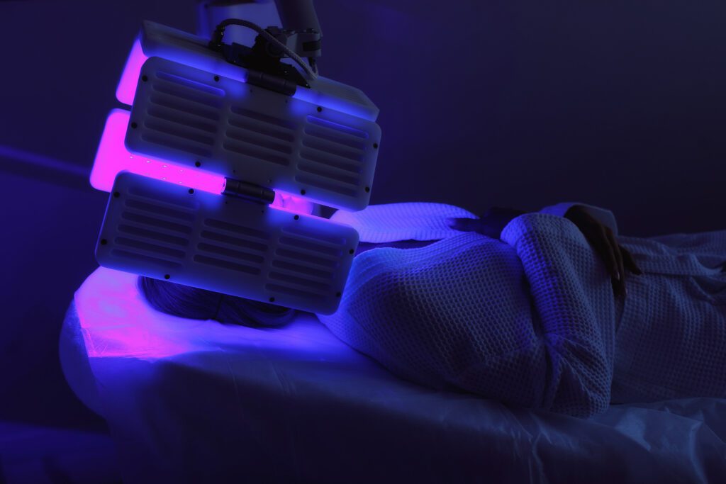 Young woman having LED light facial treatment in beauty salon. Chromotherapy, heleo4